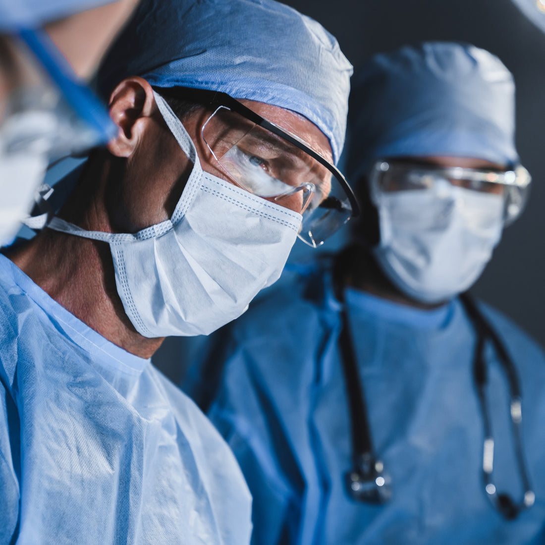Surgeons in blue scrubs and masks in an operating room.